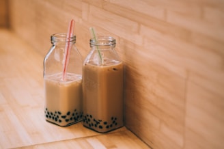 two clear glass jars with straws. milk tea and boba in each.