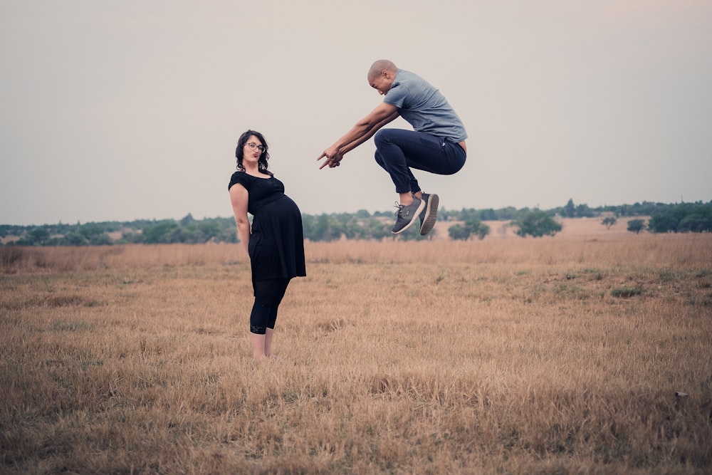 man jumping in front of woman standing on field