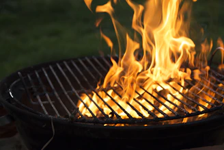 Grilled meats sizzling over glowing orange and yellow flames with a black and gold background.