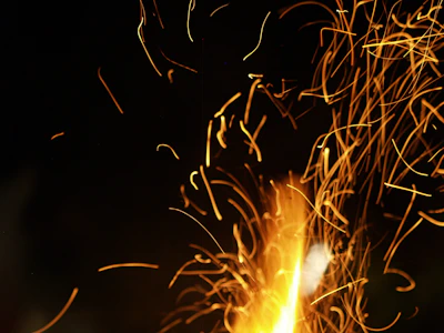 A collection of glowing orange and yellow sparks flying against a dark background, creating an energetic and dynamic visual effect.