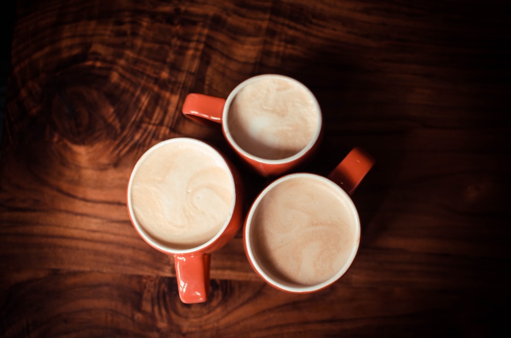 three red ceramic mugs with gray liquid inside