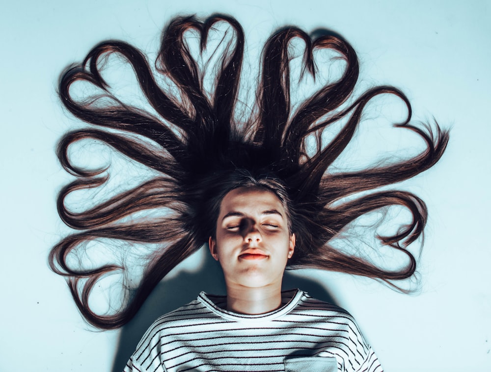 woman laying on white surface with heart forming hair