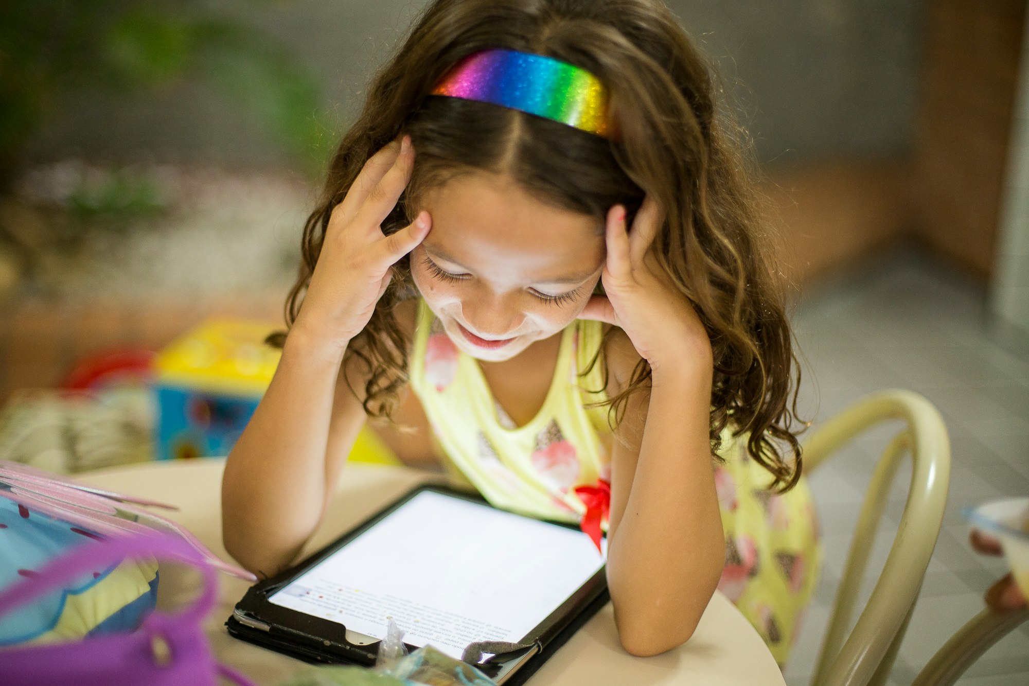 A young girl wearing a rainbow-colored headband while looking at her iPad.