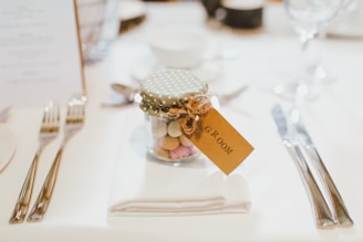 clear glass mason jar on top of white table napkin between forks and knives