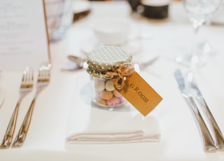 clear glass mason jar on top of white table napkin between forks and knives