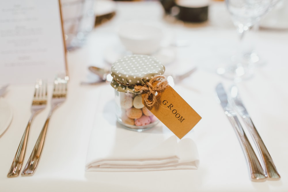 clear glass mason jar on top of white table napkin between forks and knives