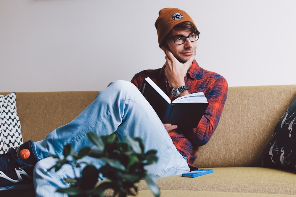 Mann sitzt auf dem Sofa und hält ein Buch in der Hand