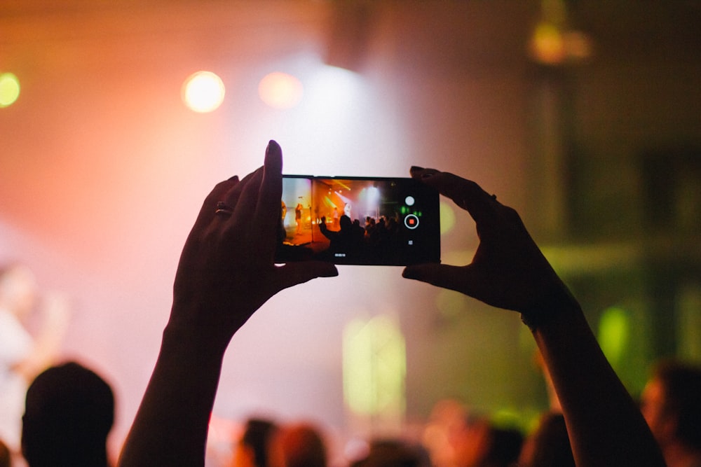 person holding smartphone while taking videos at live concert