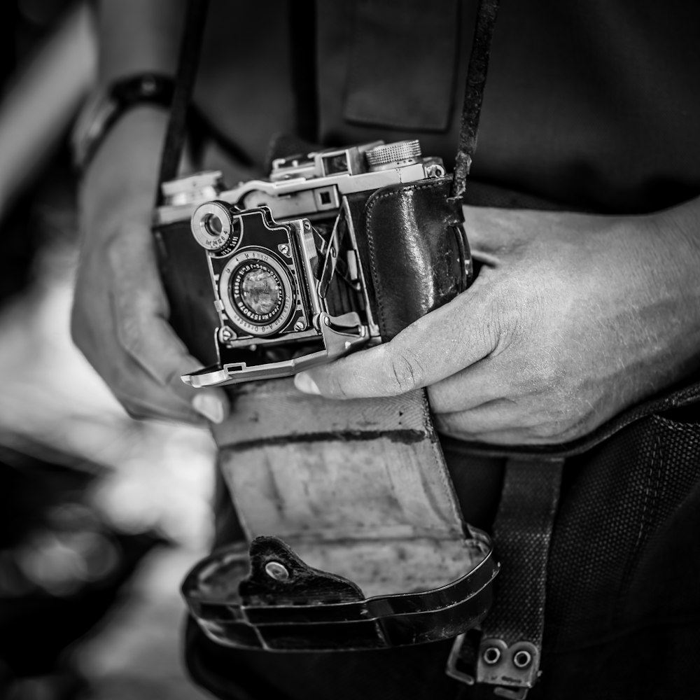 scala di grigi della persona che tiene in mano la fotocamera SLR