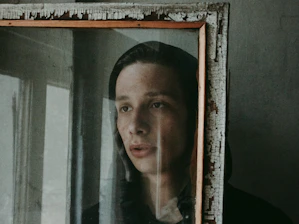 Somber person staring at a mirror reflection showing two contrasting emotional states.