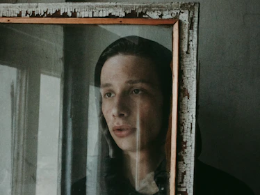 Somber person staring at a mirror reflection showing two contrasting emotional states.