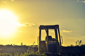 Heavy machinery smoothing a road surface at sunset, casting blue and gold hues.