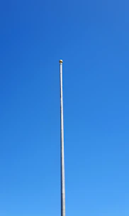 A sleek, tall aluminum flagpole standing proudly against a clear blue sky.