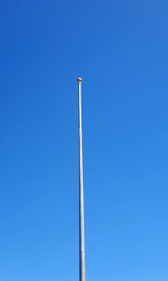 A sleek, tall aluminum flagpole standing proudly against a clear blue sky.