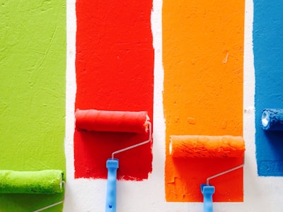 four paint rollers on a wall with different paint colors