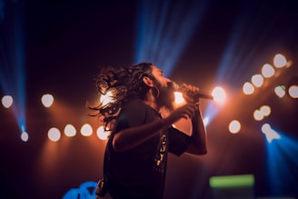 Portrait of Bea Star singing passionately on stage with colorful lights.