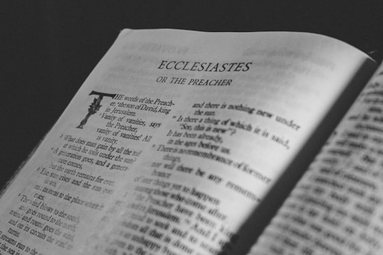 An open book displaying a page with the heading 'Ecclesiastes Or The Preacher'. The text is in a serif font and the page is lit by soft lighting, casting subtle shadows across the paper. The focus is on the content, with some parts of the text slightly blurred to create depth.