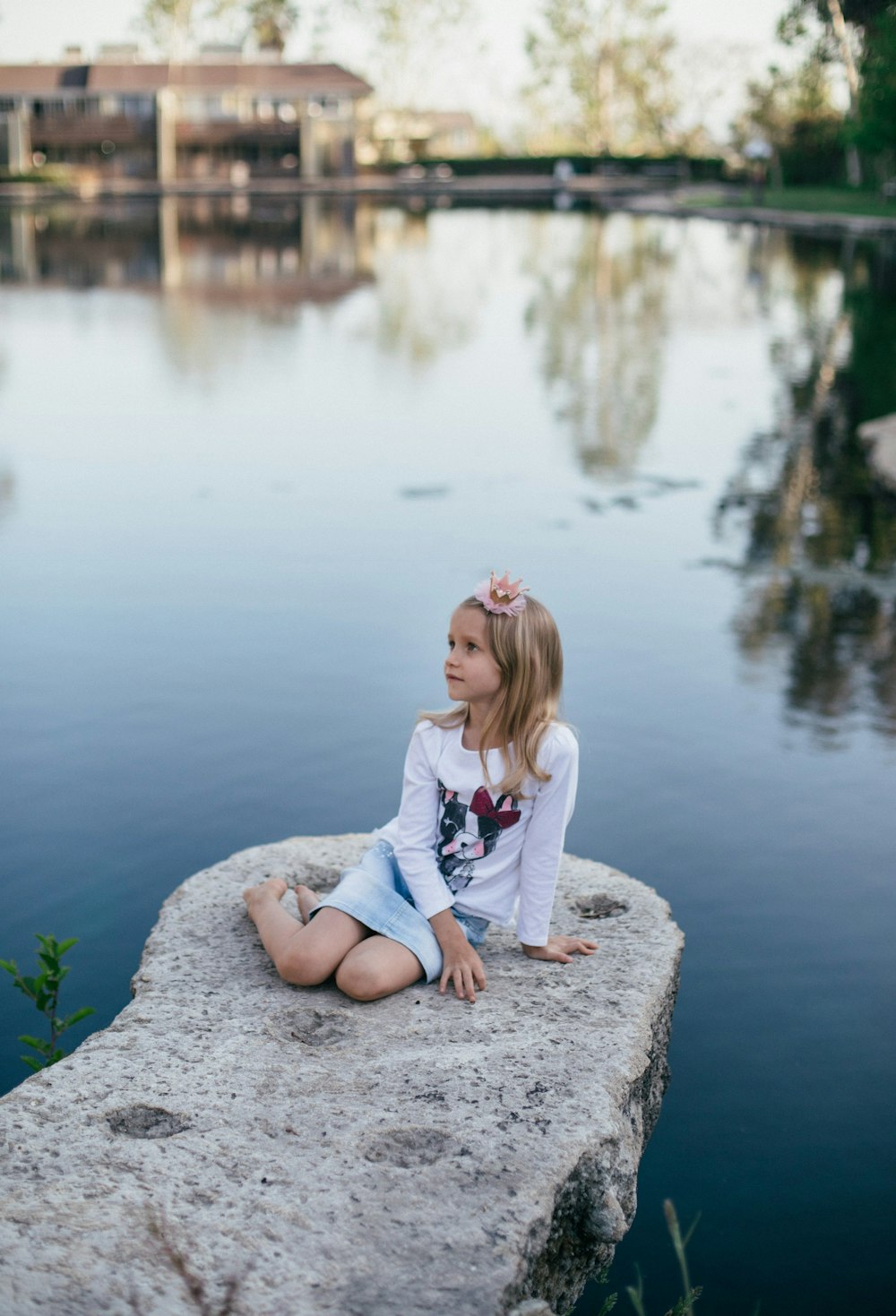 toddler girl sitting on gray stone beside body of water at daytime