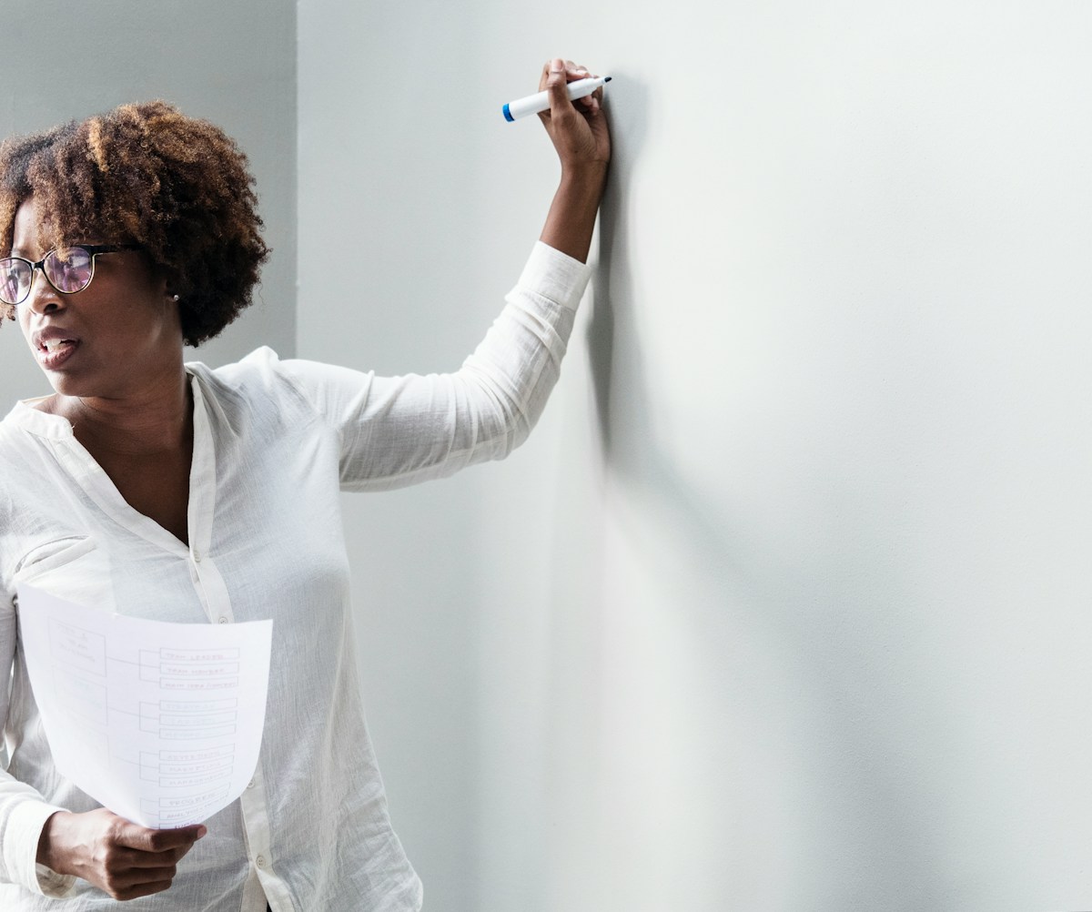 Photograph of a business woman standing in front of a blank whiteboard.