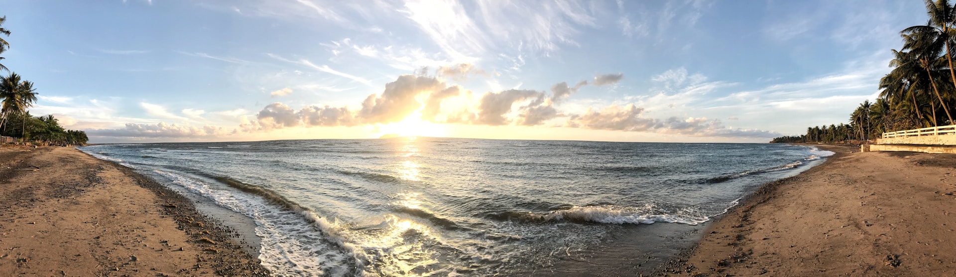 A stunning sunset view over a remote white sand beach at The Sanctuary Antigua, with gentle waves lapping the shore and palm trees swaying in the warm breeze.