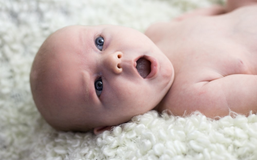 baby lying on white fur textile