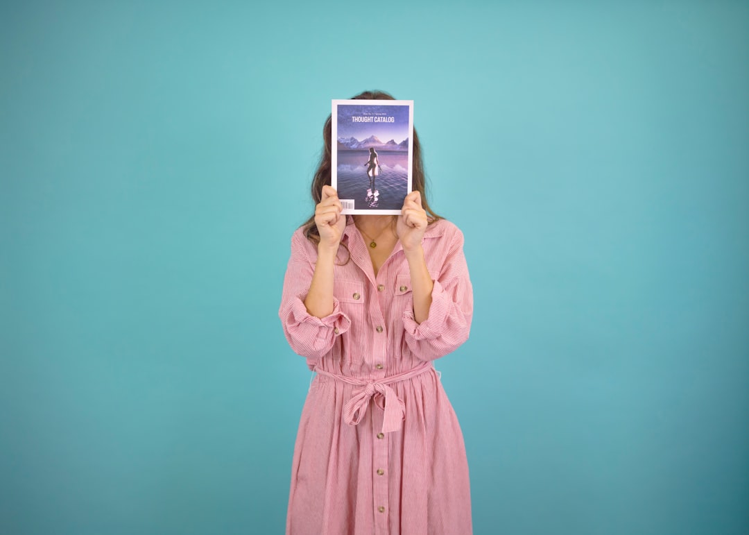 woman wearing pink dress covering her face with book