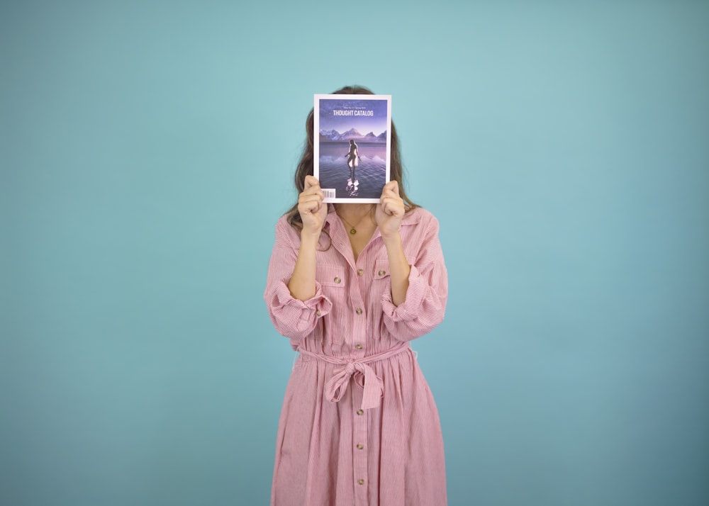 woman wearing pink dress covering her face with book