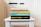 A stack of five books is neatly arranged on a white table. The books are assorted in color and size, featuring prominent titles and authors visible on their spines. The titles include 'Outliers,' 'Crucial Conversations,' 'Deep Work,' 'Getting Things Done,' and 'Tools of Titans.' The background is softly blurred, drawing focus to the books.
