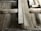 A detailed view of a wooden floor structure with overlapping planks and visible beams. The boards and beams appear weathered and aged, possibly part of a construction or renovation project. The surface shows signs of wear and some dust accumulation.