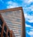 A tall modern building with numerous windows is set against a bright blue sky filled with scattered white clouds. A Canadian flag is prominently displayed on the facade of the building.