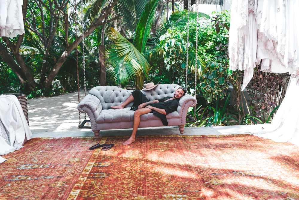 person in black robe lying on gray Chesterfield sofa