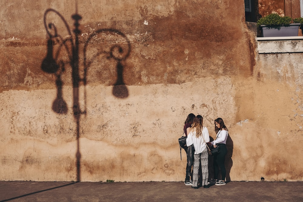 Três mulheres em pé perto da parede marrom