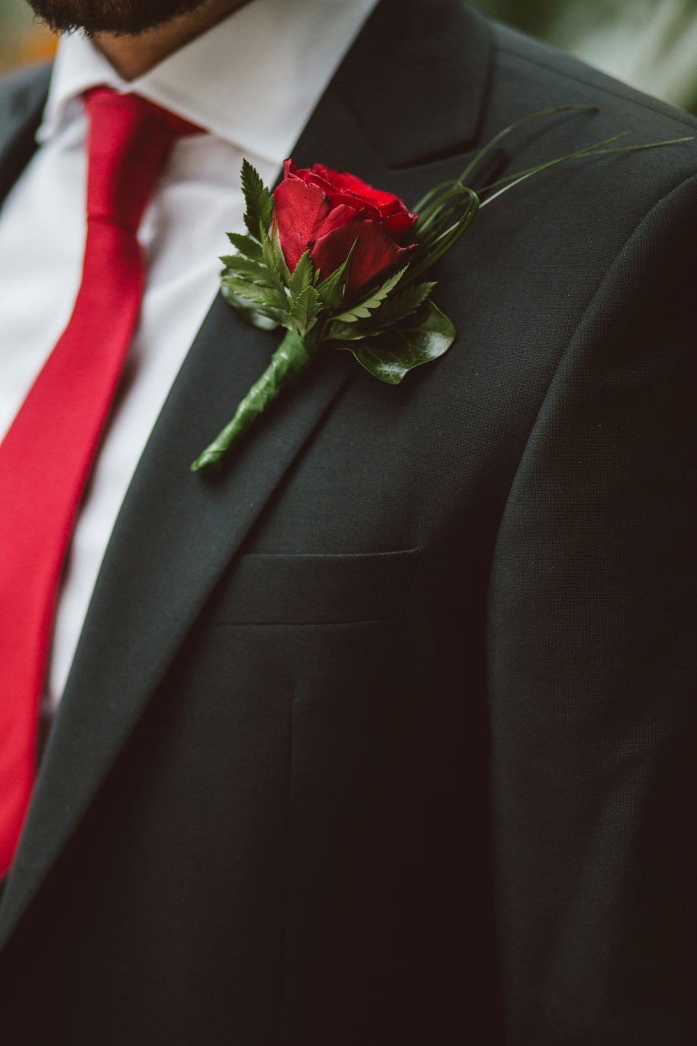 Un uomo in giacca e cravatta rossa e una boutonniere rosa