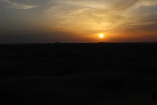 A warm sunset over the Merzouga desert with a photographer capturing the scene.