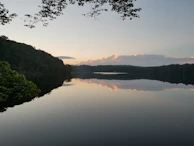 A serene lake reflecting the surrounding forest and mountains at sunset.