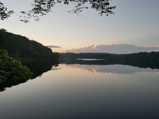 A serene lake reflecting the surrounding forest and mountains at sunset.