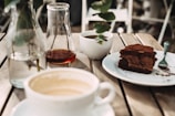 Sunlight streaming through leafy branches onto a rustic wooden table set with coffee and a slice of carrot cake.