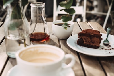 Sunlight streaming through leafy branches onto a rustic wooden table set with coffee and a slice of carrot cake.