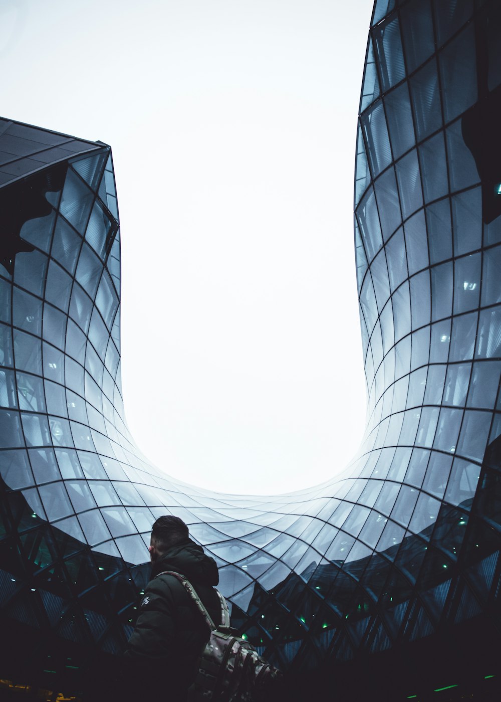 man carrying backpack white standing in front of glass building