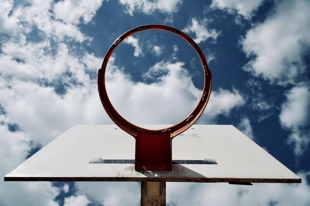 Weißer und roter Basketballkorb unter weißen Wolken und blauem Himmel am Tag