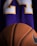 A close-up view of a textured basketball positioned in front of a purple sports jersey with the number 24 in white and yellow.