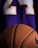 A close-up view of a textured basketball positioned in front of a purple sports jersey with the number 24 in white and yellow.