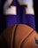 A close-up view of a textured basketball positioned in front of a purple sports jersey with the number 24 in white and yellow.