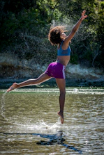 woman jumping on body of water near trees during daytime
