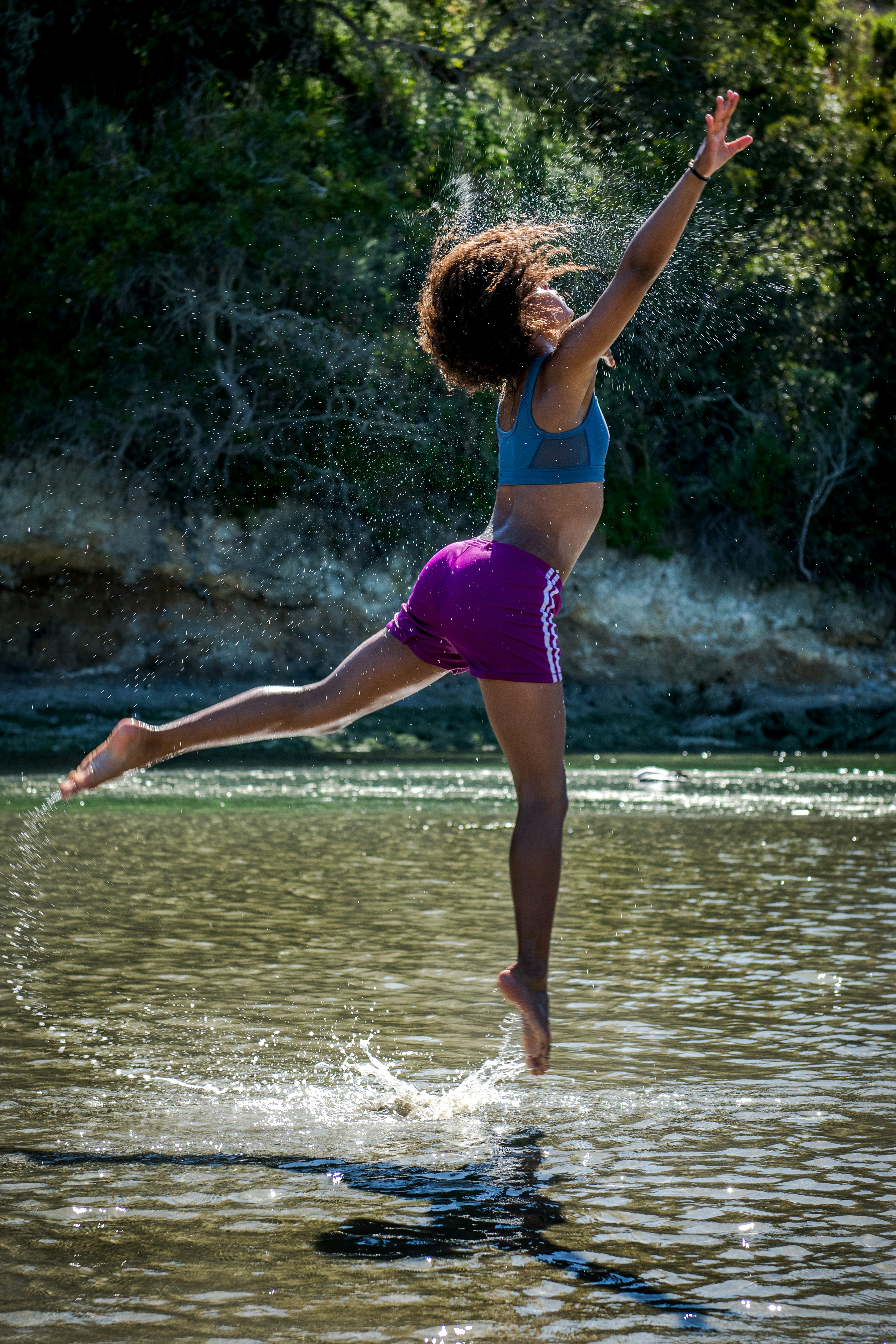 woman jumping on body of water near trees during daytime