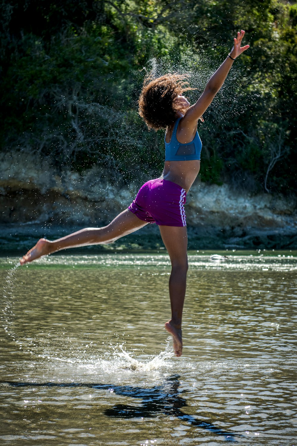 woman jumping on body of water near trees during daytime