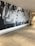 A large mural on a wall with the word 'JESUS' prominently displayed in bold letters. The background appears to feature raised hands and arms, possibly in a gesture of praise or worship. The setting seems to be a modern indoor hallway or lobby with polished concrete floors and a white ceiling.