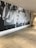 A large mural on a wall with the word 'JESUS' prominently displayed in bold letters. The background appears to feature raised hands and arms, possibly in a gesture of praise or worship. The setting seems to be a modern indoor hallway or lobby with polished concrete floors and a white ceiling.