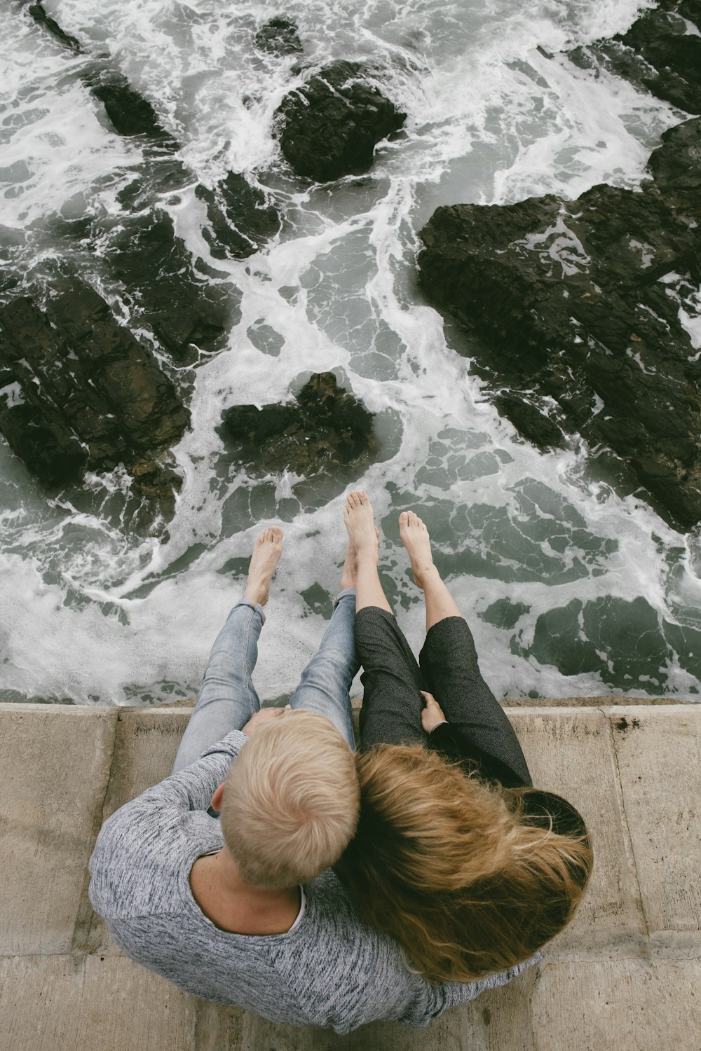 uomo e donna che si siedono sulla scogliera vicino allo specchio d'acqua