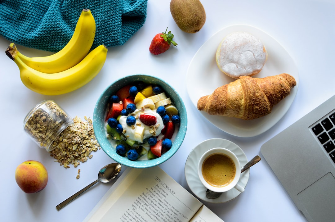 top view of strawberry and berries parfait in bowl near croissant and laptop,